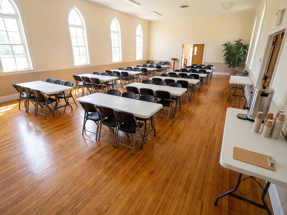 Long tables and black folding chairs in rows facing the front of a bright community hall