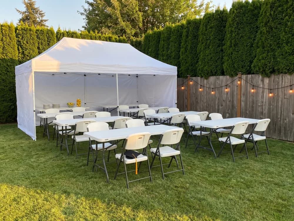 Long tables and white folding chairs under a 10 × 20 pop-up canopy on a lawn at golden hour