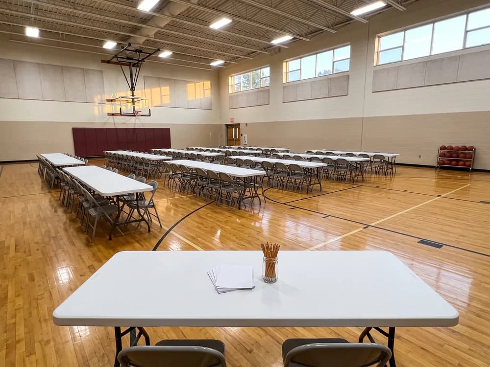 8 ft tables with silver steel folding chairs in rows across a bright school gymnasium